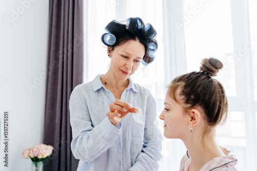 Side view of mother with curlers applying patch to teenage daughter at home photo
