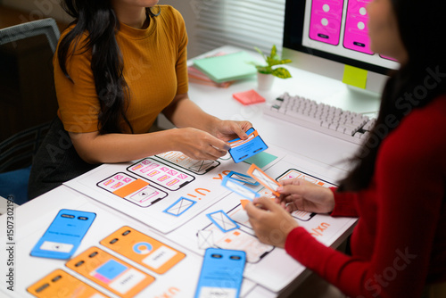 Two web designers arranging mobile application templates on a table, working together on user interface and user experience