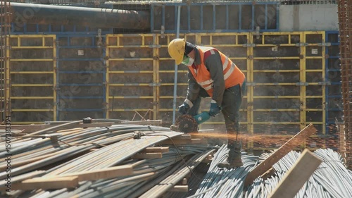 Detailed view of a laborer working at a construction site and cutting into two steel bars with a circular saw. Contractor cutting rusty metal rods with an angle grinde