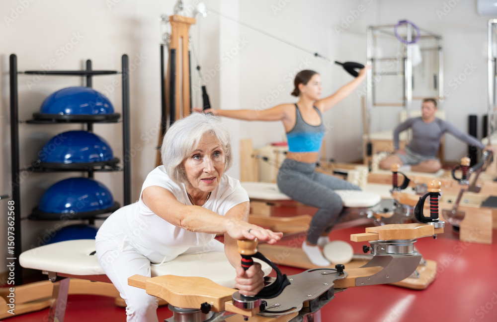 Elderly female is working on creating attractive shape of muscles of arms and body during Pilates training. Gentle and effective recovery after injuries Elderly female is working on creating attractive shape of muscles of arms and body during Pilates training. Gentle and effective recovery after injuries