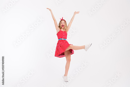 Energetic young woman in vintage polka dot dress expressing joy and freedom on white background, showcasing retro fashion and dance moves. photo