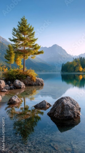 A serene lake scene with trees atop rocks reflecting on the waters surface mountains in the background under a clear sky