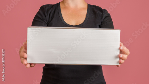 a woman stretched out a white rectangular box in front of her as a banner she is in a T-shirt on a pink background
