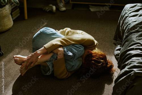 Quadro em tela Person curled up on floor, indicating emotional distress with sunlight casting o