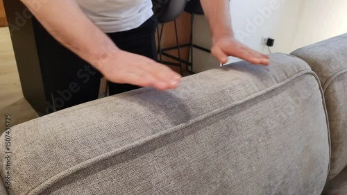 Man adjusts sofa cushion. Meticulous person smooths out wrinkles on upholstery of upholstered furniture. Men's hands in close-up. Cleanliness and neatness. Apartment cleaning