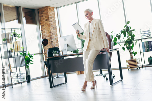 Elegant mature businesswoman in a stylish office holding a tablet, showcasing professionalism and confidence in a modern workplace