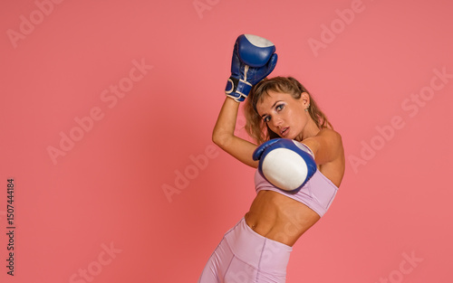 woman with a beautiful muscular figure in sportswear and boxing gloves on her hands posing on a pink background, copy space