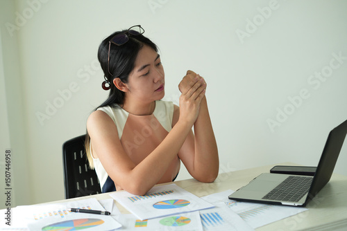 An asian business lady working for a long time and typing the computer and preparing the contract, so her wrist is hurt and massaging her hurt wrist by another hand, overloaded and office syndrome.	