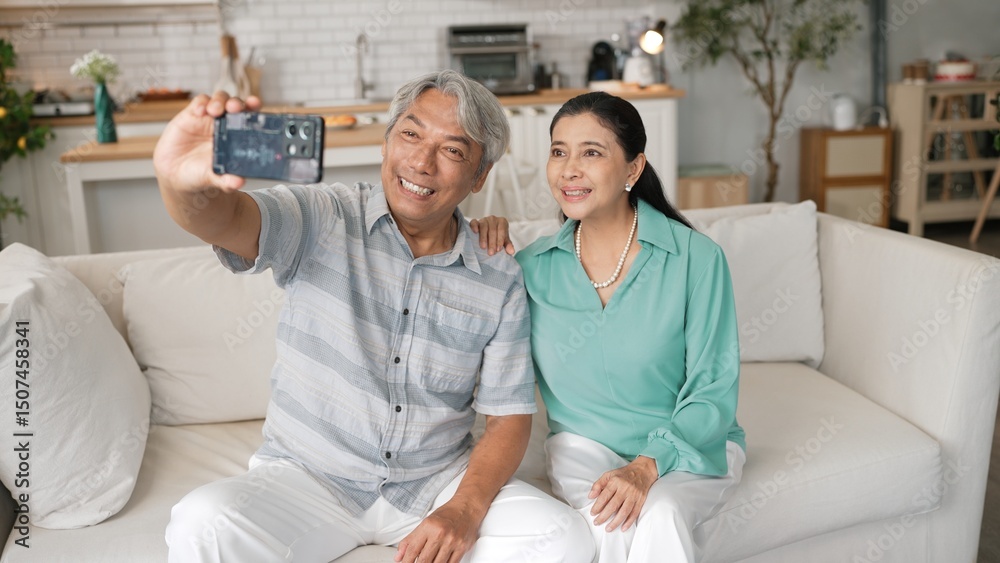 Obraz premium Happy grandfather and grandmother making video call with their son at home. Elder man holding smart phone and sitting at sofa while old woman greeting with cheerful vibe at modern house. Myrmidon.