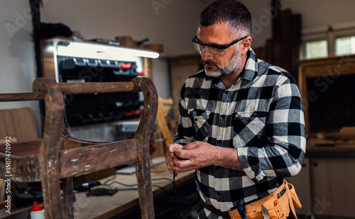 Carpenter standing in his workshop restoring old piece of furniture.