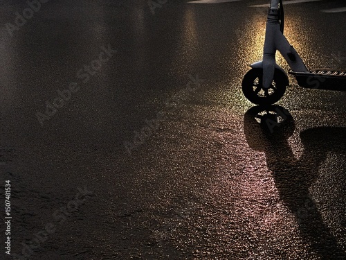 Electric scooter reflecting on wet asphalt at sunset