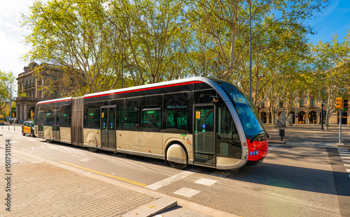 Modern Articulated City Bus Driving Through Tree-Lined Street in Barcelona
