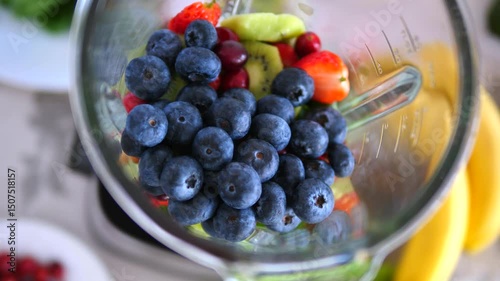 Fresh blueberries are added to a blender already containing chopped kiwi, strawberries, and cranberries, ready to be blended into a healthy smoothie