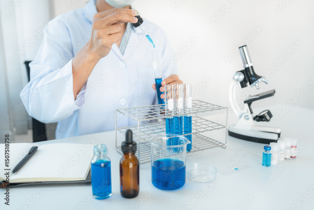 Fototapeta premium Scientist woman in protective face mask dropper to dropping blue liquid into test tube while working