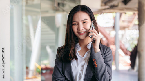 Asian businesswoman in suit, smiling and answer call with client on smartphone to talking about new business project