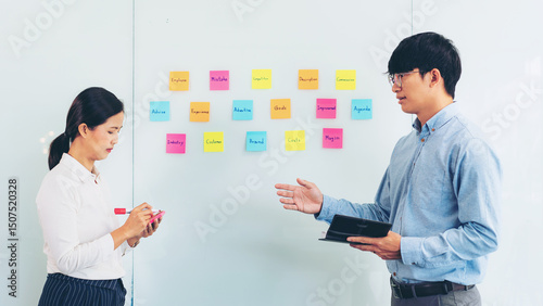 Two business executive team holding and taking notes keyword on board wall to brainstorm about a new business project for planning marketing plan together in the office