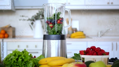 Fresh berries, spinach, and other fruits are placed in a blender, ready to be mixed into a healthy smoothie, surrounded by various fruits and vegetables on a kitchen counter