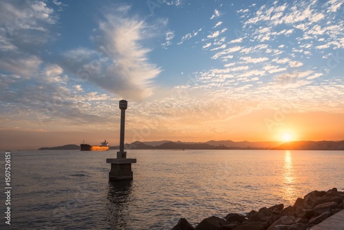 Santos city, Brazil. Colorful sunset in the bay. The Portuguese Standard Monument in the foreground and a cargo ship entering the Santos port channel.
