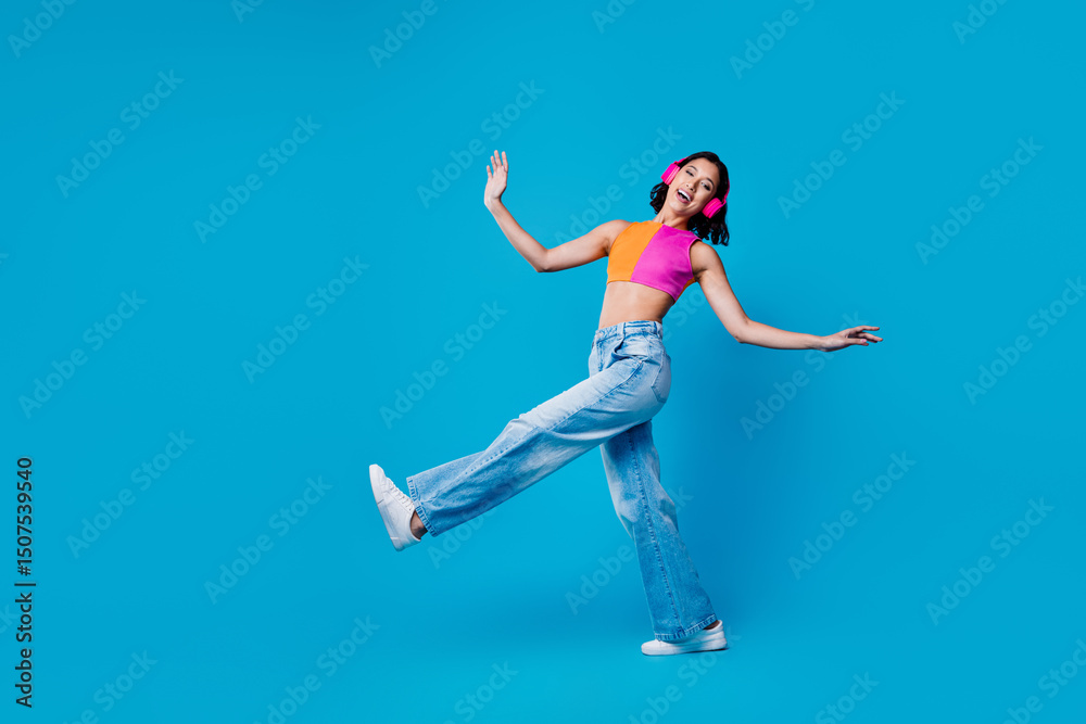 Obraz premium Young stylish woman enjoying music and dancing with headphones against a vibrant blue background