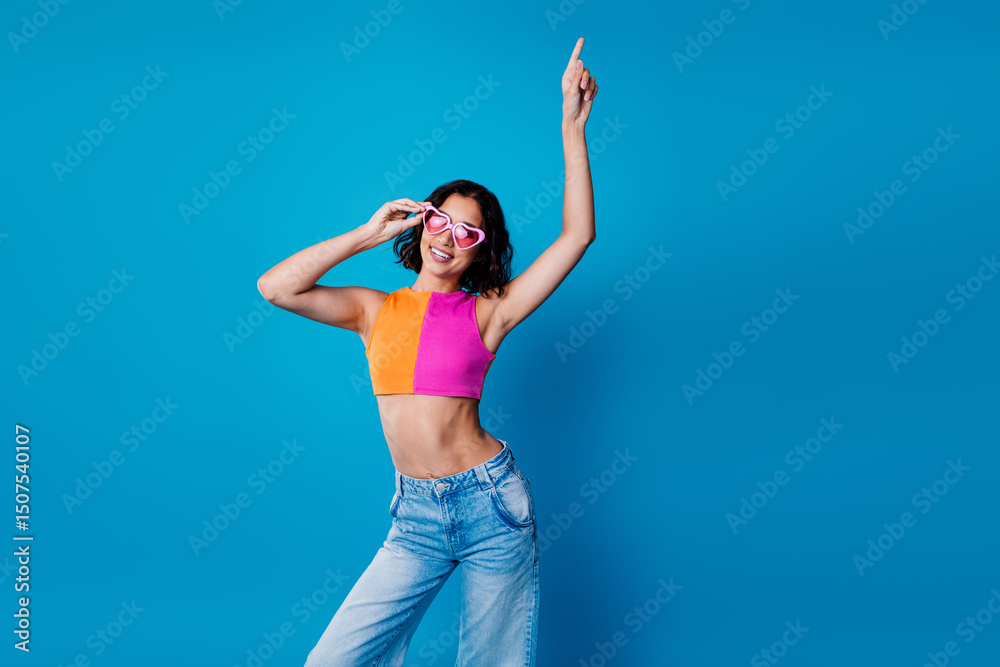 Naklejka premium Trendy young woman with vibrant outfit posing energetically against a bright blue background, embodying fun and youthfulness.