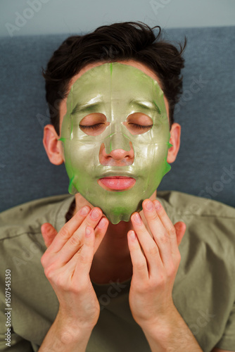 Relaxed man with hydrating face mask at home. Man is applying facial mask for rejuvenate complexion, skincare concept.