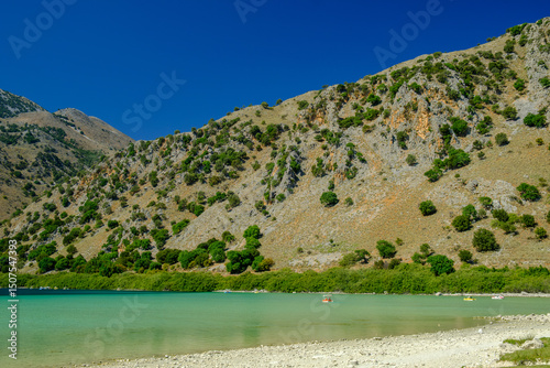 Clear turquoise waters of Lake Kournas with mountainous landscape under blue sky in Crete, Greece