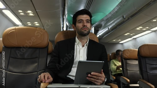 Business Travel. Businessman in a suit travels on airplane working on a tablet and speaking on the phone. Modern international business trip. Inflight digital tech connectivity. Global Business travel