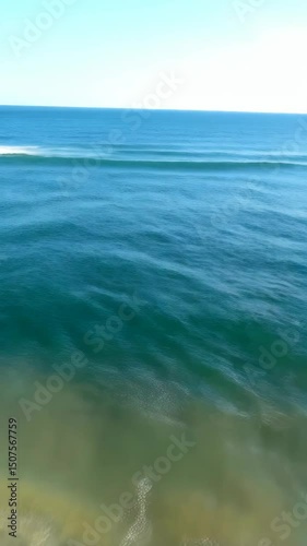 Waves crashing on sandy beach under clear sky with clouds in open coastal scene