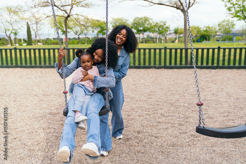 Mother and aunt joyfully pushing their niece on a swing in a vibrant playground, creating cherished memories on a sunny day