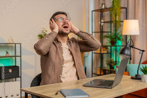 Caucasian young businessman freelancer shouting, trying not to hear the loud noise from neighbor apartment in building while they renovate home and he cant work on laptop netbook because of the noise.