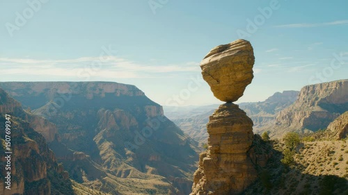 Balanced rock formation above a canyon landscape under clear sky.