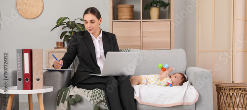 Young happy business mother working with laptop and little baby on sofa at home