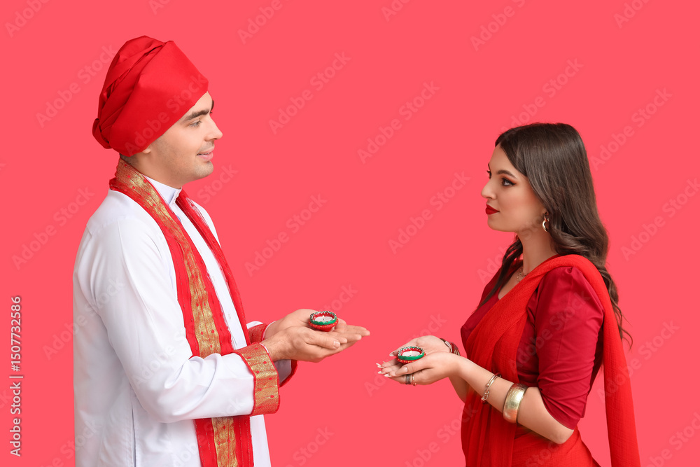 Beautiful Indian couple with diya lamps on red background Beautiful Indian couple with diya lamps on red background