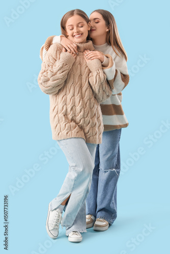 Young lesbian couple in warm sweaters hugging on blue background