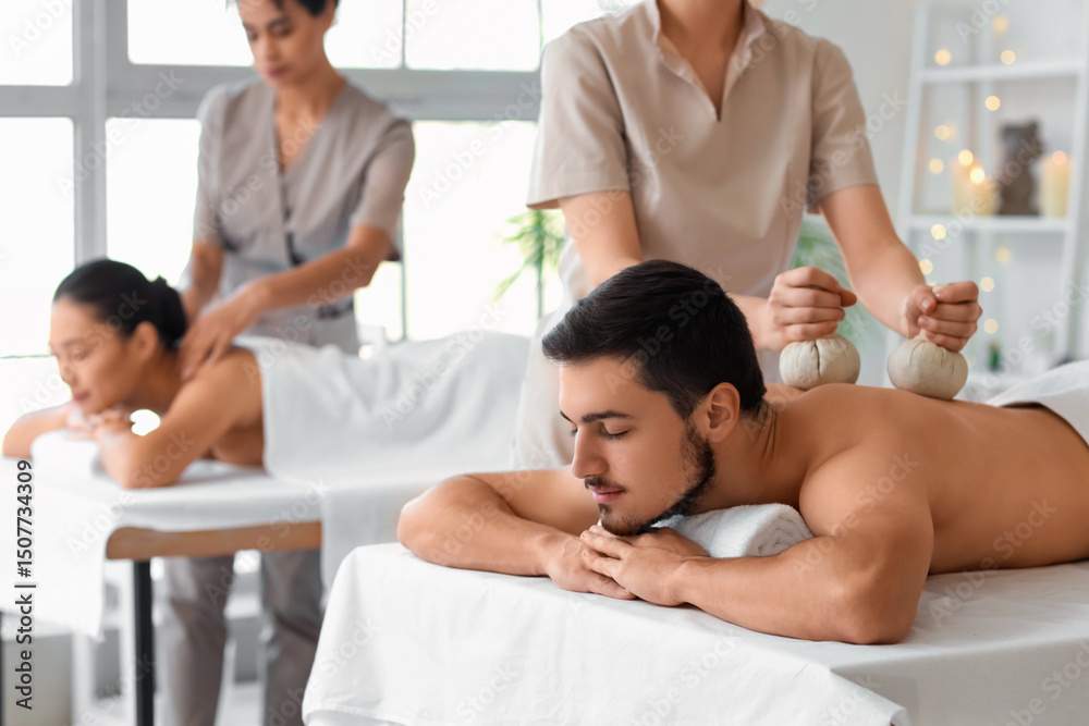 Fototapeta premium Young man getting massage with herbal bags in spa salon