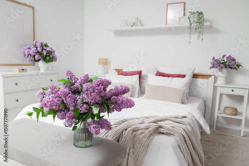 Interior of light bedroom with lilac flowers in vases