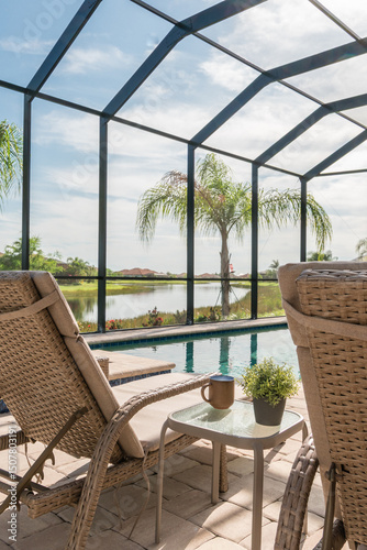 Lounge chair beside blue swimming pool in suburban Florida home with screened enclosure and palm trees.
