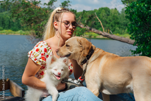 Young beautiful woman with blond hair playing with her labrador retriever dog and Pomeranian puppy on the lake shore