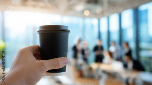 Wallpaper Mural Hand holding a black takeaway coffee cup in a modern office with a blurred background of people in a business meeting.
 Torontodigital.ca