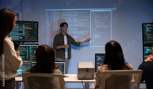 Asian man presents code using a projector during a software development meeting or coding workshop, guiding attendees through problem-solving and programming concepts in an educational setting.