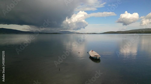 A tranquil lake scene features a solitary boat with stunning clouds enhancing the peaceful atmosphere
