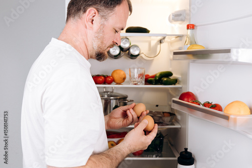 Fotografie Man inspecting fresh eggs in refrigerator while preparing for a nutritious break
