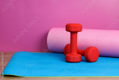 Red dumbbells and pink foam roller resting on blue yoga mat: promoting health and fitness photo