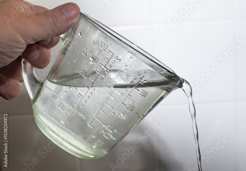 Measuring cup pouring water with precision, captured mid-action to highlight kitchen tools, liquid measurement, hydration, and culinary preparation.