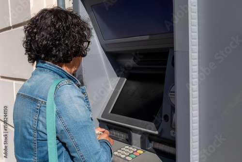 Woman is using an ATM machine. She is wearing a blue jacket. The ATM has a black screen