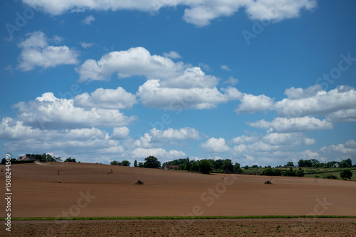 Large field with a few trees and a house in the distance. The sky is mostly clear with a few clouds scattered throughout