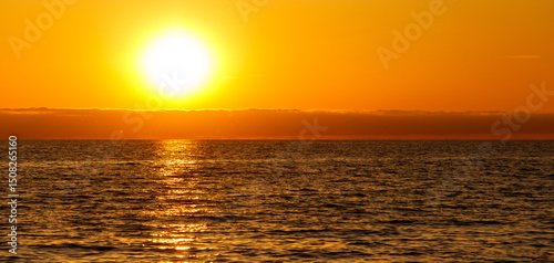 The sun is setting over the ocean, casting a warm glow on the water