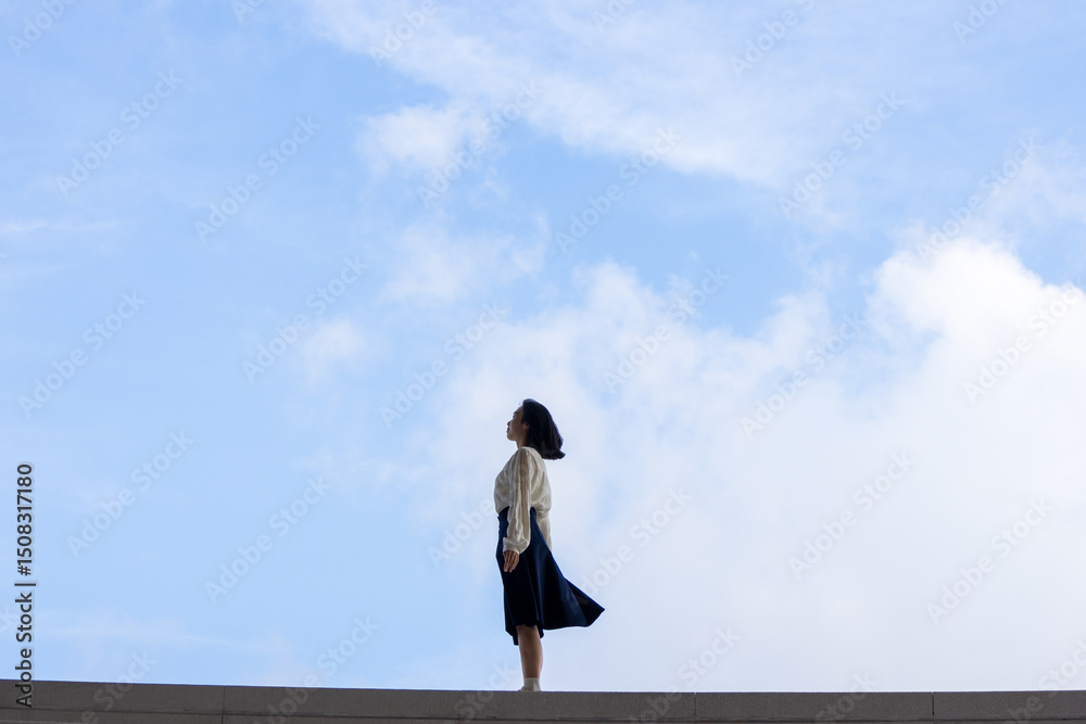 A young woman is on the steps under the blue sky and white clouds A young woman is on the steps under the blue sky and white clouds