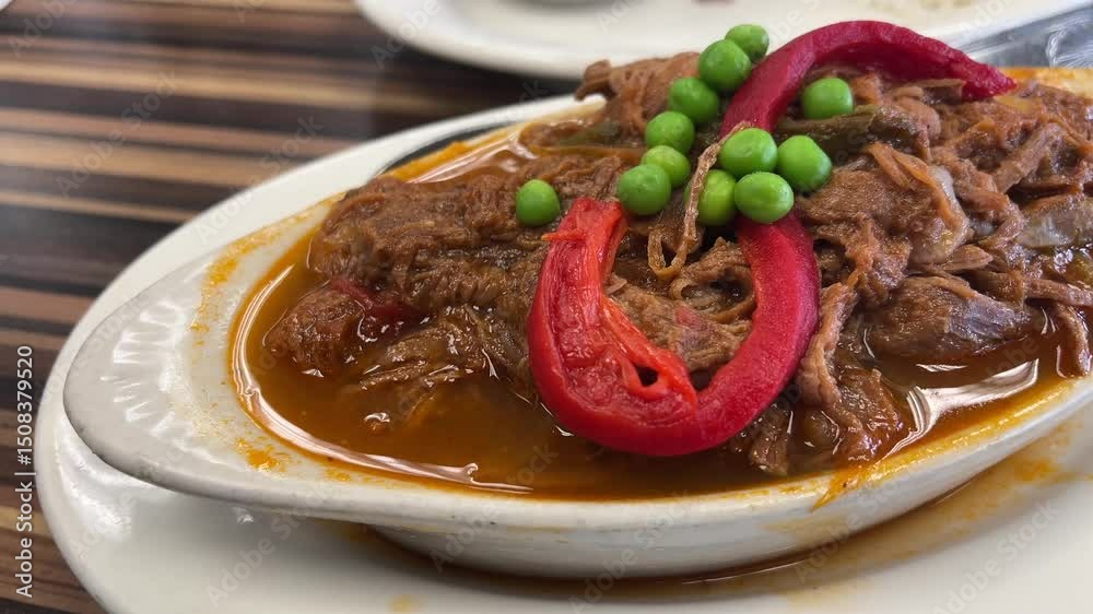 Close-up of Ropa Vieja, a savory Cuban dish with shredded beef in a rich tomato sauce, garnished with green peas and red bell peppers
