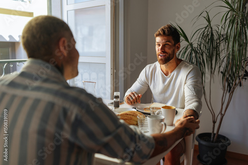 Gay couple holding hands and having breakfast at home